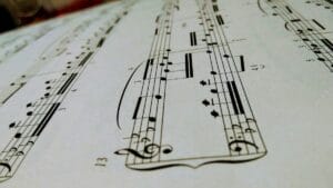 Mano de un músico realizando una transcripción musical al escribir notas con un lápiz sobre una partitura en blanco.